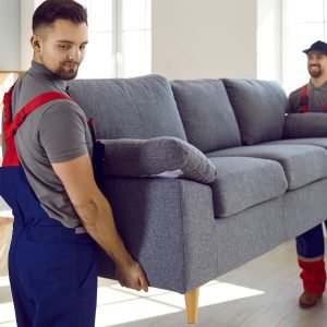 Two,Professional,Relocation,Service,Workers,In,Overalls,Move,Sofa,In